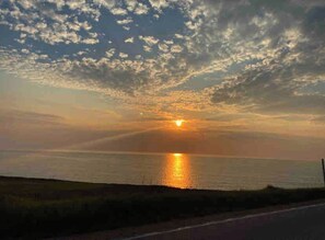 Ein Sonnenuntergang über einem Gewässer, im Vordergrund eine Straße.