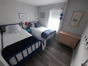 Ein Schlafzimmer mit zwei Betten, einer Holzkommode und einem Fenster mit Vorhängen.