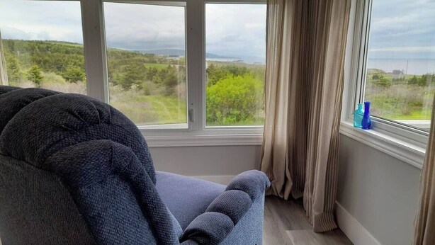 Een kamer met een groot raam, een donkerblauwe fauteuil en uitzicht op groen en heuvels.