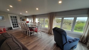 Een ruime woonkamer met een eettafel, stoelen en een groot raam met uitzicht op groen.