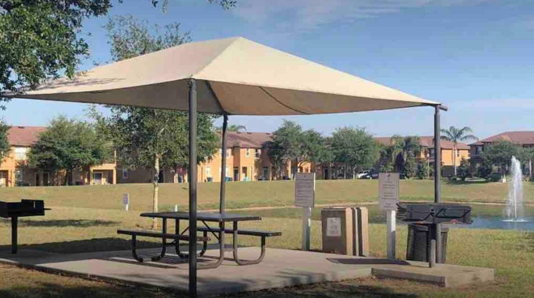 En plats för picknick med ett bord och en bänk under ett tak, omgiven av en gräsyta och en fontän.