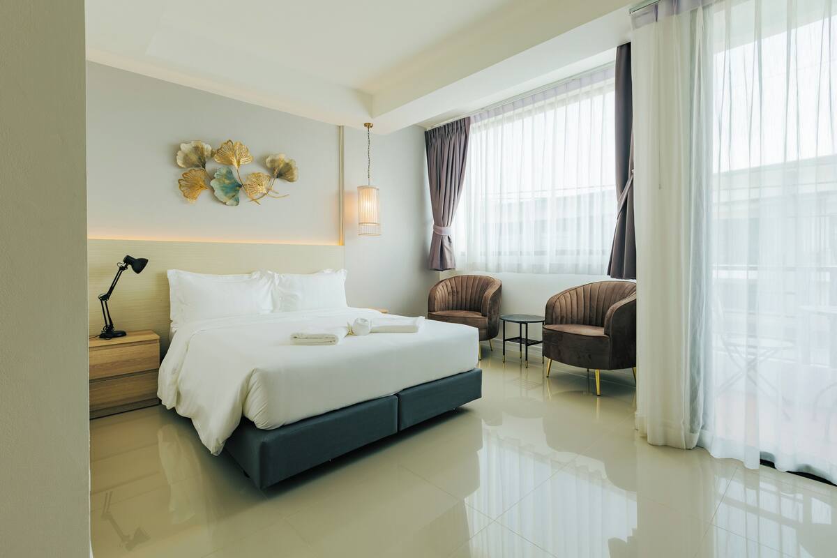 Una habitación de hotel moderna con una cama grande, un escritorio, dos sillas y un elemento decorativo en la pared.