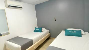 A hotel room with two single beds, a small bedside table, a mirror, and an air conditioning unit on the wall.