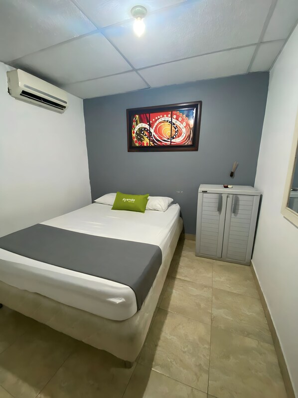 Un dormitorio con cama, aire acondicionado, un armario y una obra de arte colgada en la pared.