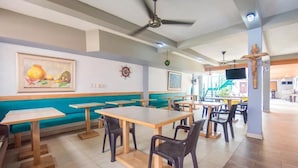 A restaurant with wooden tables and chairs, a blue cushioned bench, and a crucifix on the wall. - Hotel Puerto Vigia Inn (Cartagena)