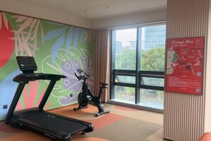 A gym with a treadmill, stationary bike, and a large window with a view of buildings and trees. - Orange Hotel (Suzhou Dushu Lake Xi'an Jiaotong-Liverpool University) (Suzhou)