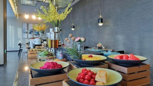 Uma área de jantar moderna com uma mesa comprida posta com frutas, legumes, caixas de madeira e luminárias pendentes.