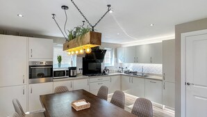 A modern kitchen with white cabinets, a wooden dining table, and a hanging light fixture. - Sheffield Charming Detached 4bd Home (Catcliffe)