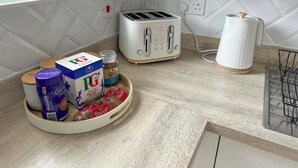 A kitchen with a white tiled backsplash, a toaster, a kettle, and a tray with food items. - Sheffield Charming Detached 4bd Home (Catcliffe)