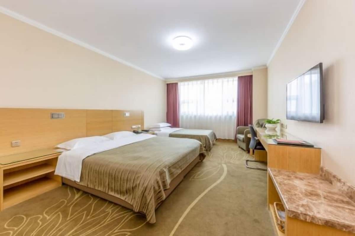 Habitación de hotel con dos camas, un escritorio, una silla, un televisor y una ventana con cortinas.