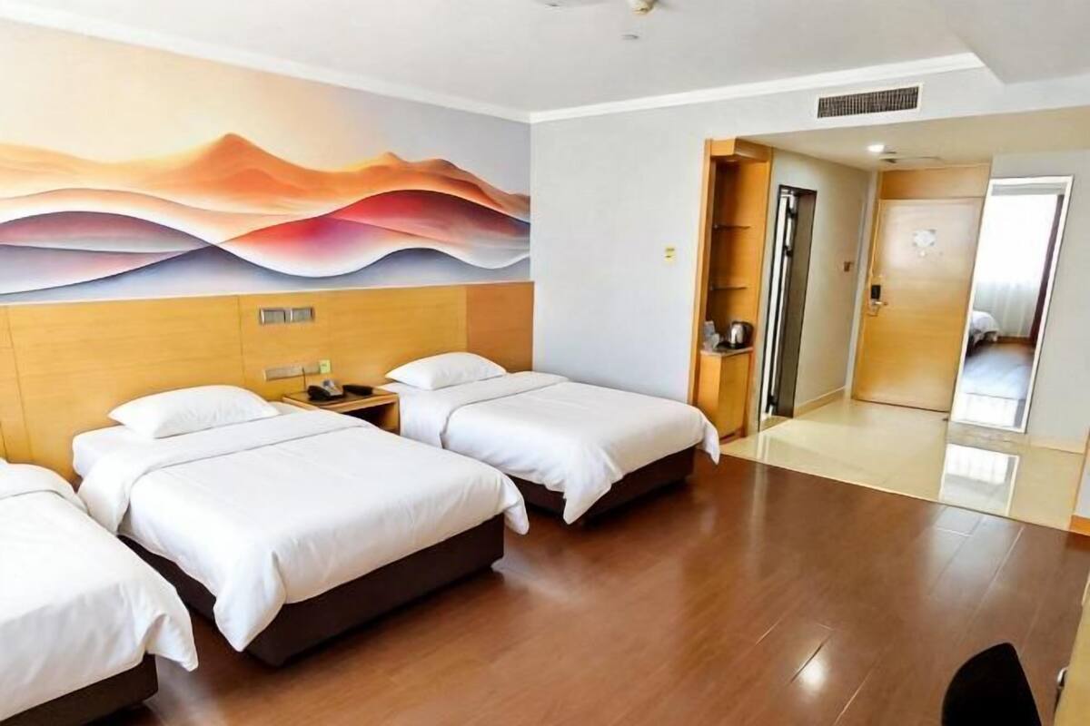 Una habitación de hotel con tres camas, un cabecero de madera, un mural abstracto moderno y suelo de madera.