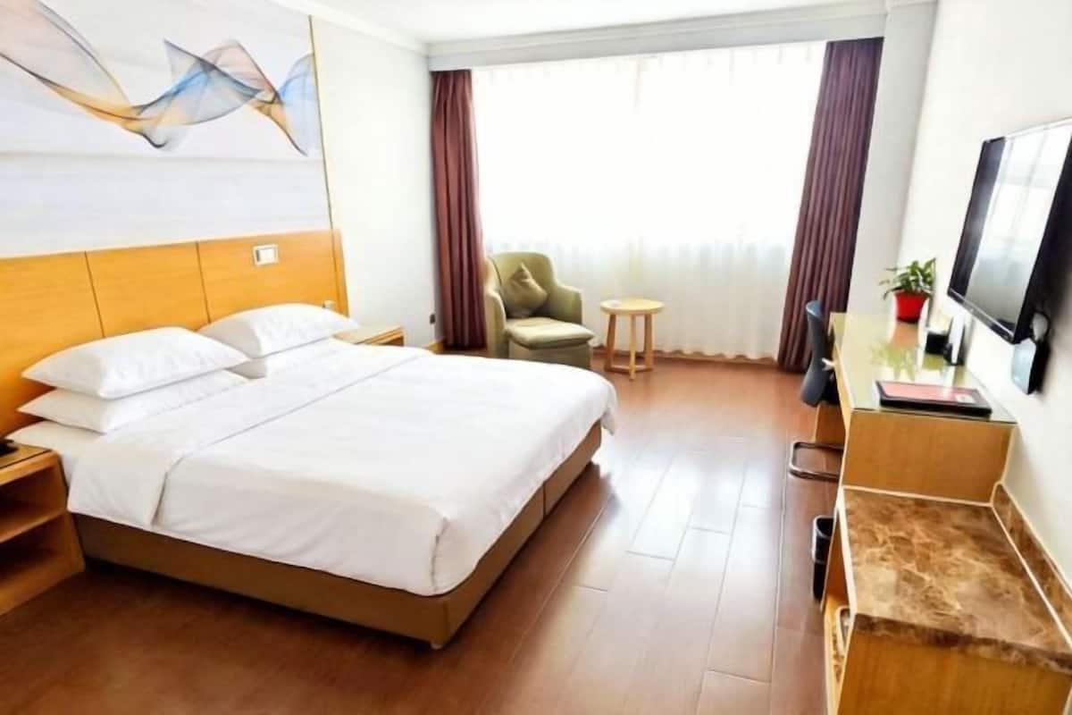Una habitación de hotel con cama, televisión, escritorio, silla y ventana con cortinas.