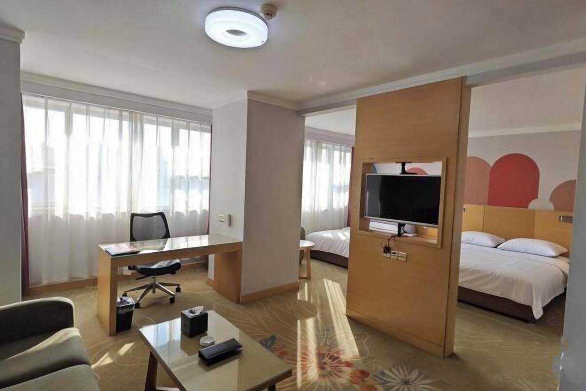 Habitación de hotel con cama, escritorio, silla, televisor y una ventana grande con cortinas.