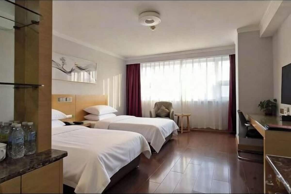 Habitación de hotel con dos camas, un escritorio, una silla, una mesita y un ventanal grande con cortinas.