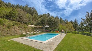 A rectangular swimming pool with stone tiles, surrounded by a grassy lawn, with a play area and umbrellas in the background. - Villa in Cortona with 2 bedrooms sleeps 4 (Cortona)