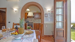 A dining area with a table set for a meal, a kitchen in the background, and a view of the outdoors through an open door. - Villa in Cortona with 2 bedrooms sleeps 4 (Cortona)