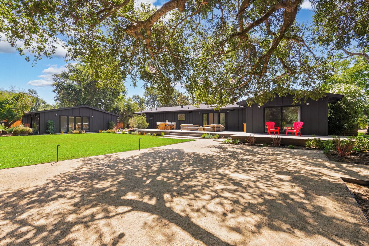 A modern house with a covered patio, red chairs, and a well-maintained lawn.