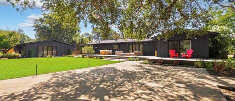 A modern house with a covered patio, red chairs, and a well-maintained lawn.