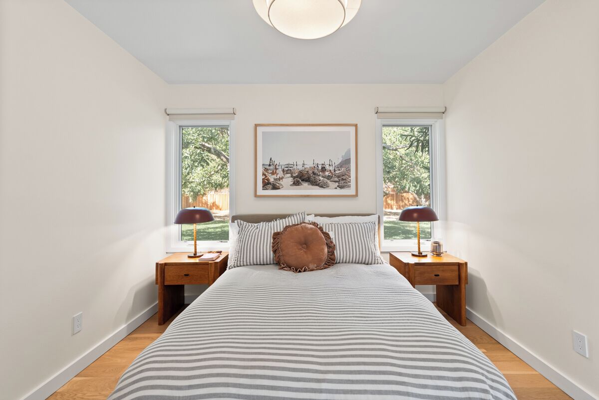 Une chambre à coucher avec un grand lit, deux tables de chevet, un tableau encadré au mur et deux fenêtres.
