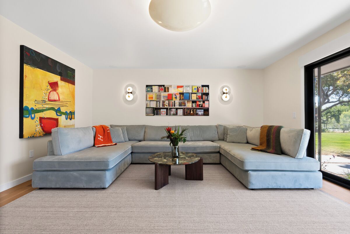 A modern living room with a sectional sofa, a coffee table with a vase, a bookshelf, and a large abstract painting.
