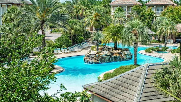 Um resort com uma piscina grande, rodeado por palmeiras e vista para o oceano.