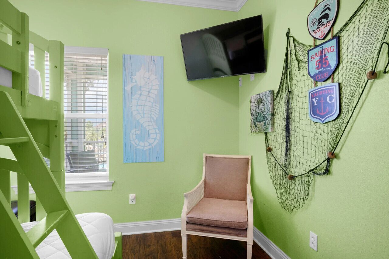 Une pièce avec un mur vert, un lit, une chaise, un téléviseur et une décoration en forme de filet.