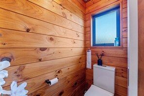 Une salle de bain rustique, aménagée dans une cabane en bois, avec des toilettes, une fenêtre et un petit lavabo.