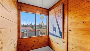A wooden cabin room with a large window, wooden walls, and a ceiling light fixture. - Riverside Haven - Turangi Holiday Home (Turangi)