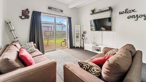 A modern living room with two sofas, a TV, and a sliding glass door leading to a balcony. - Riverside Haven - Turangi Holiday Home (Turangi)