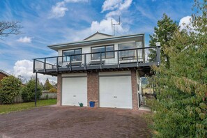 Une maison à deux étages avec un balcon, deux portes de garage et une allée pavée en briques.