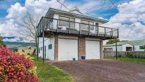 A modern two-story house with a balcony, garage doors, and a paved driveway. - Riverside Haven - Turangi Holiday Home (Turangi)