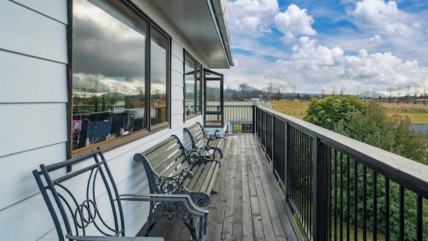 A wooden deck with benches, overlooking a park and a body of water. - Riverside Haven - Turangi Holiday Home (Turangi)
