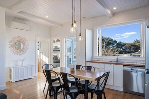 Una cocina moderna con una mesa de comedor de madera, sillas negras, una ventana con vistas a árboles y un lavavajillas empotrado.