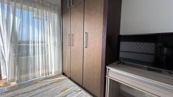 Une pièce avec une grande armoire, un téléviseur posé sur un meuble et des rideaux légers à la fenêtre.