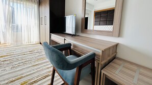 Ein modernes Hotelzimmer mit Schreibtisch aus Holz, einem blauen Sessel, einem großen Spiegel und einem Fernseher.
