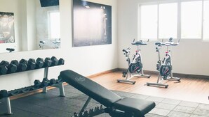 Ein Fitnessraum mit Trainingsgeräten, einer Bank, Kurzhanteln und einem großen Spiegel.