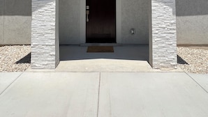 Ein Gebäudeeingang mit steinverkleideter Fassade, einer dunklen Tür und einem kleinen Vordach über der Tür.