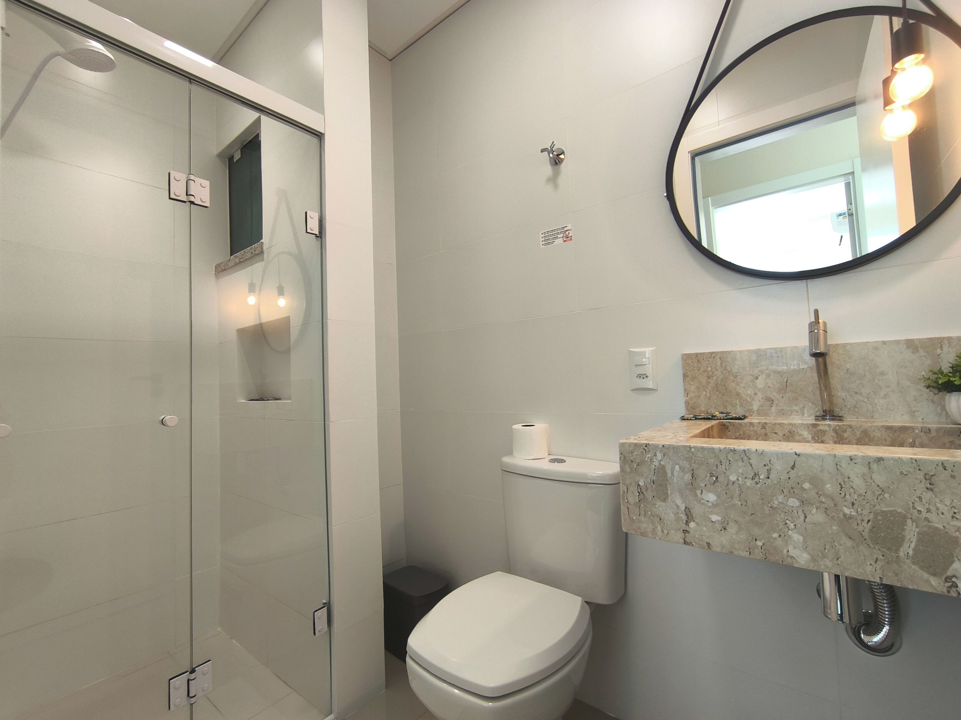 A modern bathroom with a glass shower enclosure, a toilet, and a sink with a marble countertop.