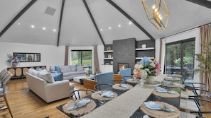 A spacious living area with a fireplace, sofas, dining table, and large windows.