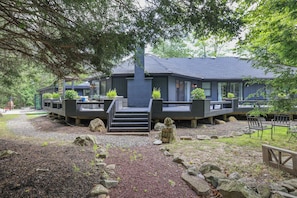 A modern building with a dark exterior, a covered outdoor area with seating, and a stone pathway leading to the entrance.