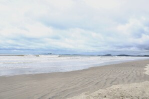 A beach with a wide sandy shore and gentle waves. - Pousada 1 minute from the beach | UNR (Cabo Frio)