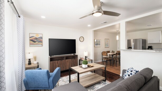 A modern living room with a flat-screen TV, a ceiling fan, and a dining area with a kitchen in the background. - Fab 2B/2Bth, All New  & Easy Access  to US99 (Fresno)