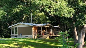 A single-story mobile home with a porch, surrounded by trees and grass.