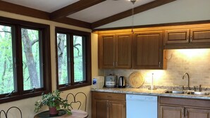 A kitchen with wooden cabinets, a dishwasher, and a ceiling fan. There is a window with a view of trees and a table with chairs.