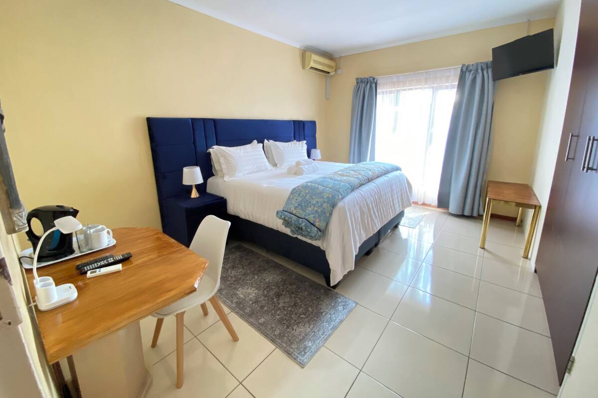 A hotel room with a bed, bedside table, lamp, and a desk with a chair.