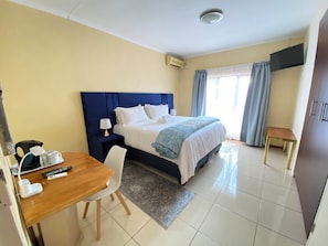A hotel room with a bed, bedside table, lamp, and a desk with a chair. - Mokolodi Hide out (Gaborone)