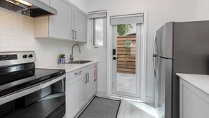 Una cocina moderna con armarios blancos, un refrigerador de acero inoxidable, un horno empotrado y una ventana con vista a una cerca de madera.