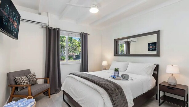 Un dormitorio moderno con cama, mesitas de noche, una silla y una ventana con cortinas.