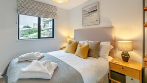 A hotel room with a bed, two bedside tables, a window with a view, and a hanging light fixture. - 2 Bed in Woolacombe (oc-c29617) (Woolacombe)