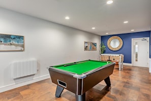 A pool table in a room with a blue accent wall, a mirror, and framed artwork.